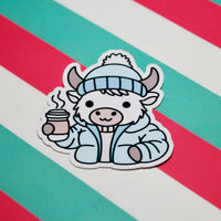 Load image into Gallery viewer, Cozy Winter Cow Blue Coat Sticker – Cute Highland Cow Vinyl Sticker – Hot Drink Cow – Glossy Waterproof Sticker – Winter Aesthetic – 4.5cm x 4.99cm

