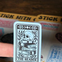 Load image into Gallery viewer, Card with 'The Reader' design held over a box of stickers.
