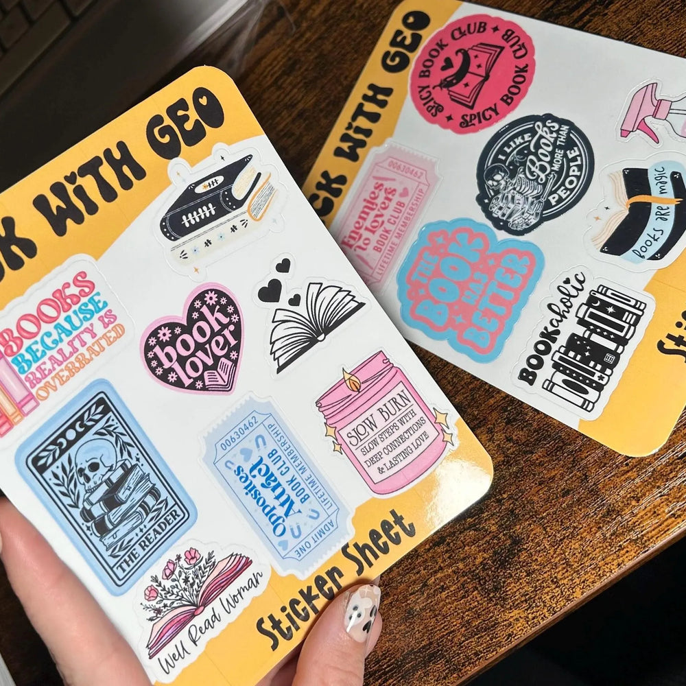 Two sticker sheets with various designs held by a hand on a wooden surface.