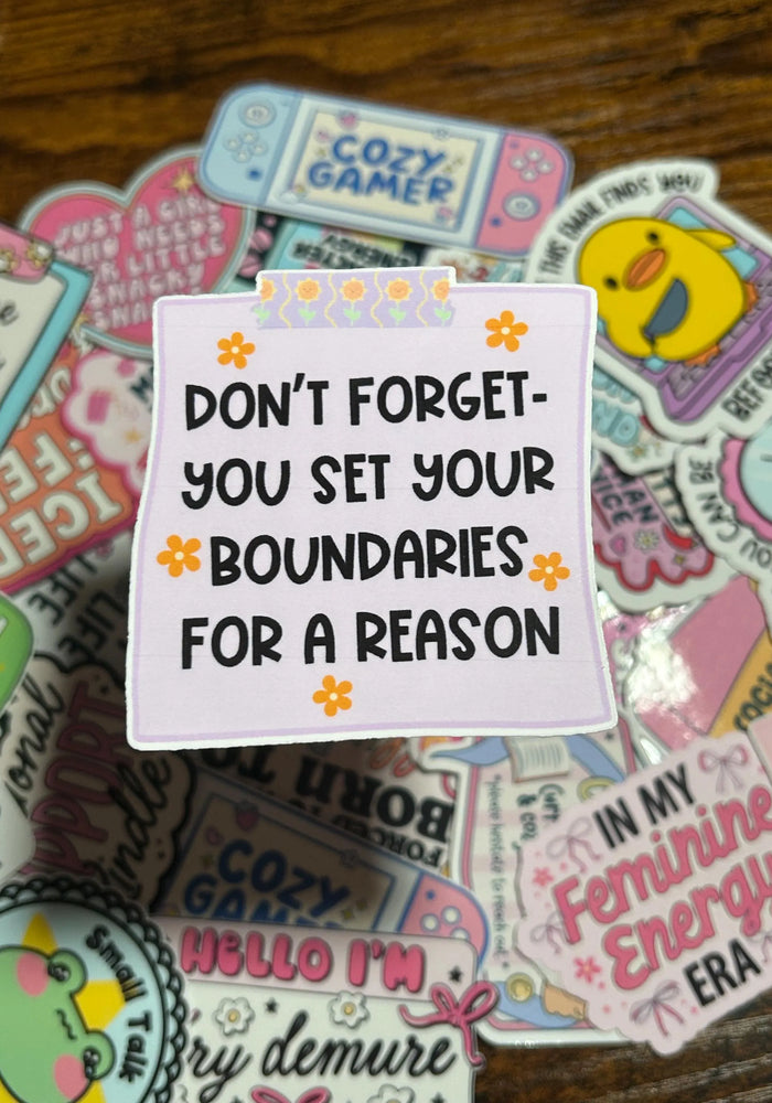 Stack of colourful stickers with motivational text on the main Sticker, Yellow Flowers around the text on the purple Sticker. On a wooden surface