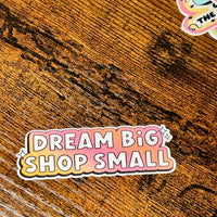 Load image into Gallery viewer, Sticker with 'Dream Big Shop Small' text on a wooden surface
