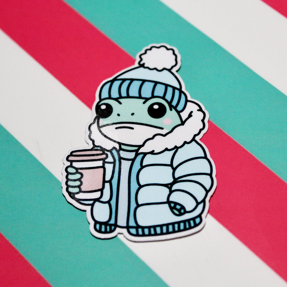 Cute Winter Frog Blue Coat Sticker – Cozy Frog in Puffer Jacket – Frog with Hot Drink – Glossy Waterproof Vinyl Sticker – Pastel Winter Aesthetic – 3.64cm x 5.5cm