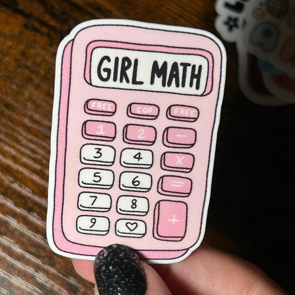Sticker of a pink calculator with 'Girl Math' text held by a hand on a wooden surface.