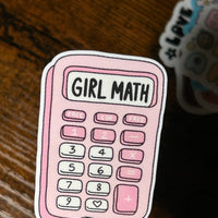 Load image into Gallery viewer, Sticker of a pink calculator with 'Girl Math' text held by a hand on a wooden surface.
