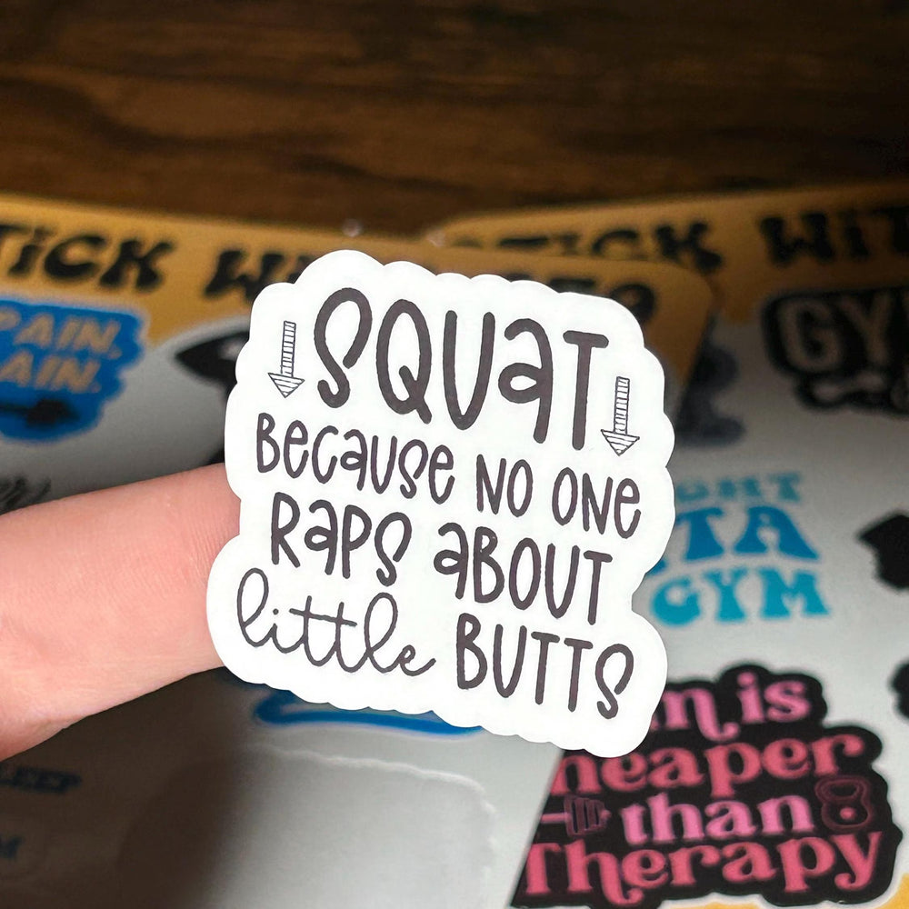 Sticker with text 'Squat because no one raps about little butts' held by a hand.