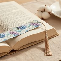 Load image into Gallery viewer, Open book with a floral bookmark on a wooden surface with a cup of tea and glasses.
