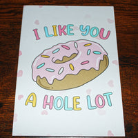 Load image into Gallery viewer, Card with a donut illustration and text 'I like you a hole lot' on a wooden surface.

