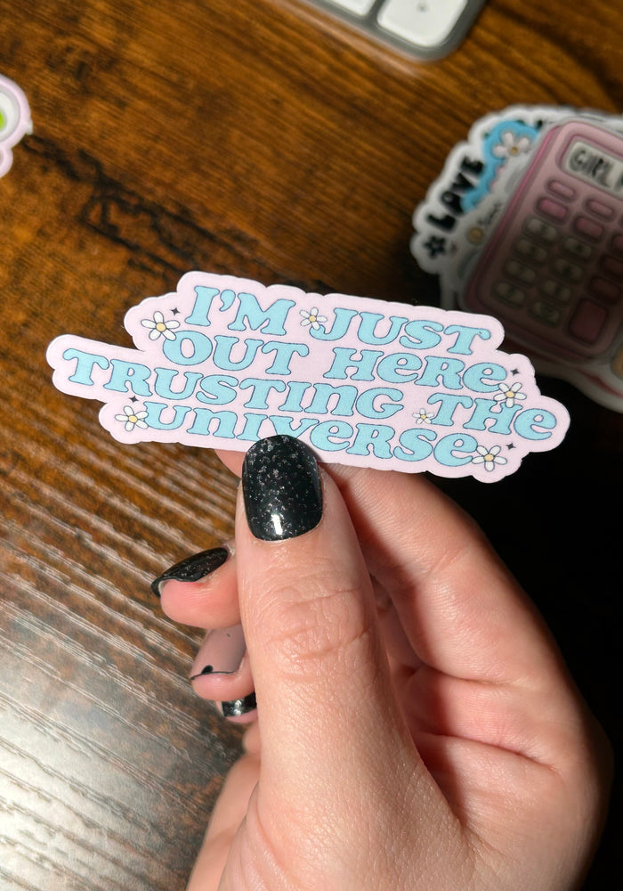 Hand holding a pink sticker with text on a wooden surface