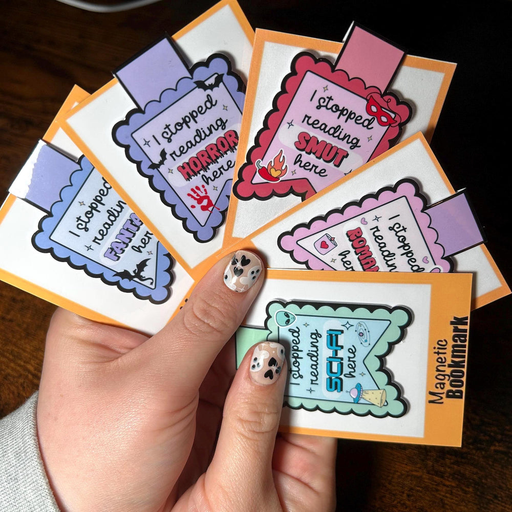 Hand holding a stack of colorful bookmarks with humorous text on a wooden surface.