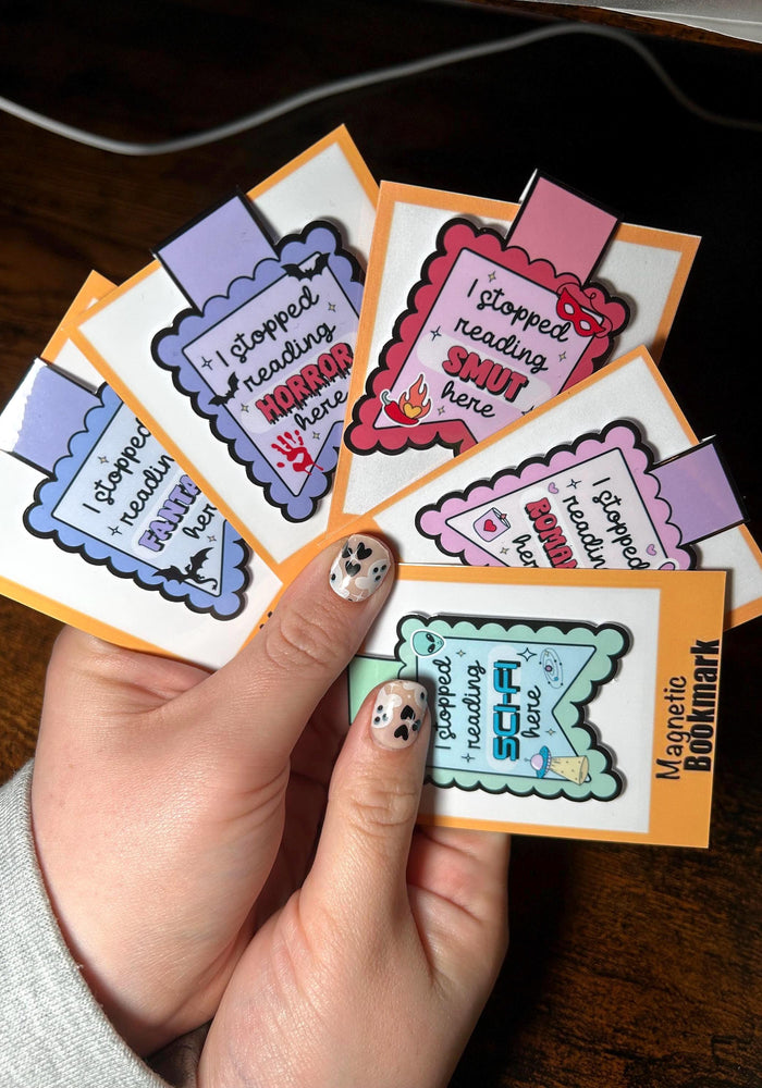 Hand holding a stack of colorful bookmarks with humorous text on a wooden surface.