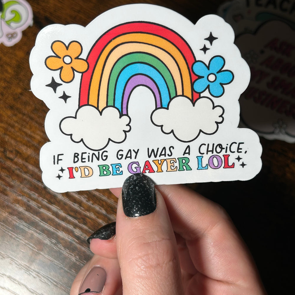 Sticker with rainbow and flowers held by a hand on a wooden surface