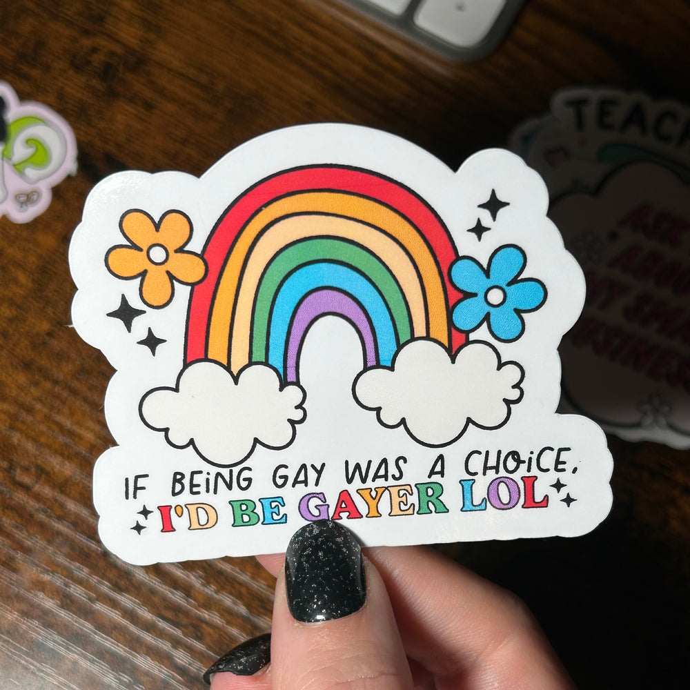 Sticker with rainbow and flowers held by a hand on a wooden surface