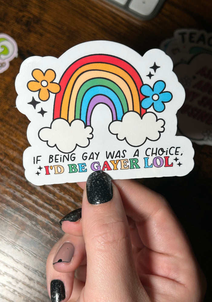 Sticker with rainbow and flowers held by a hand on a wooden surface