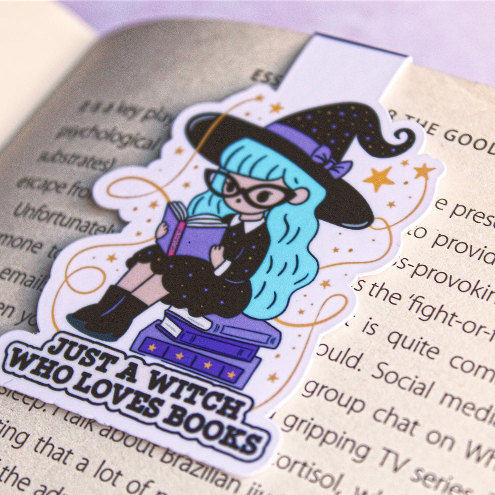 bookmark of a witch with blue hair and glasses holding a book, placed on an open book.