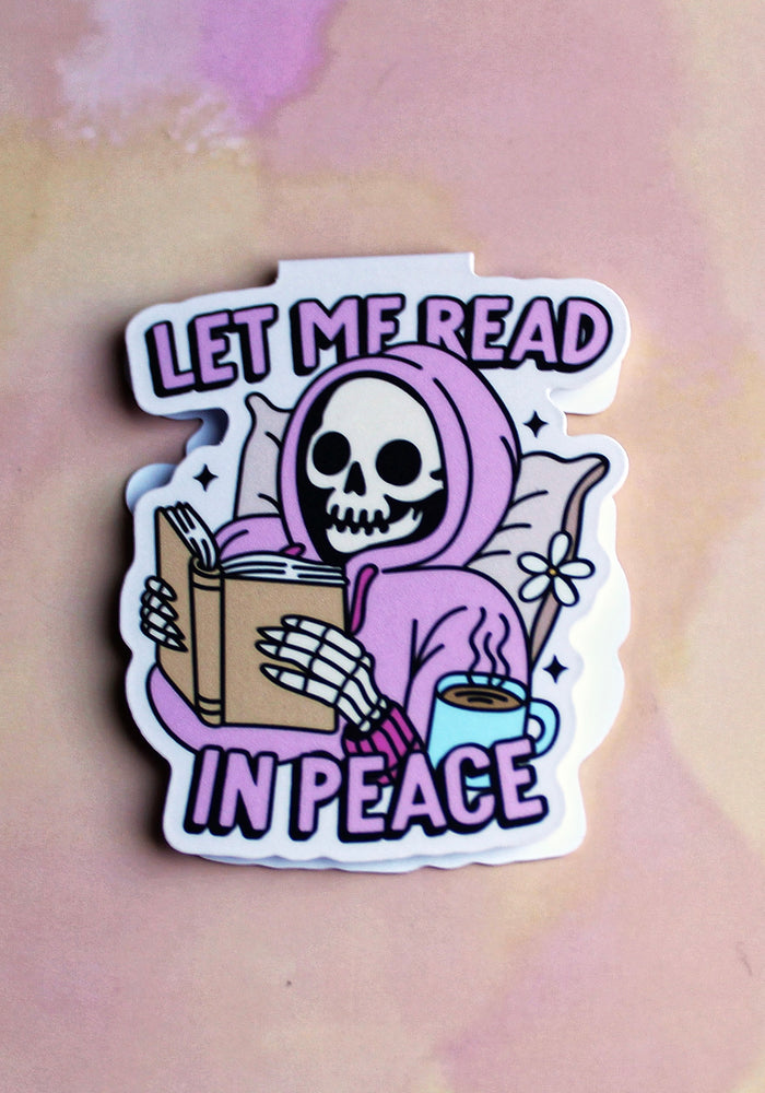 bookmark with a skeleton reading a book and a cup of coffee, text 'Let me read in peace', on a pastel background.