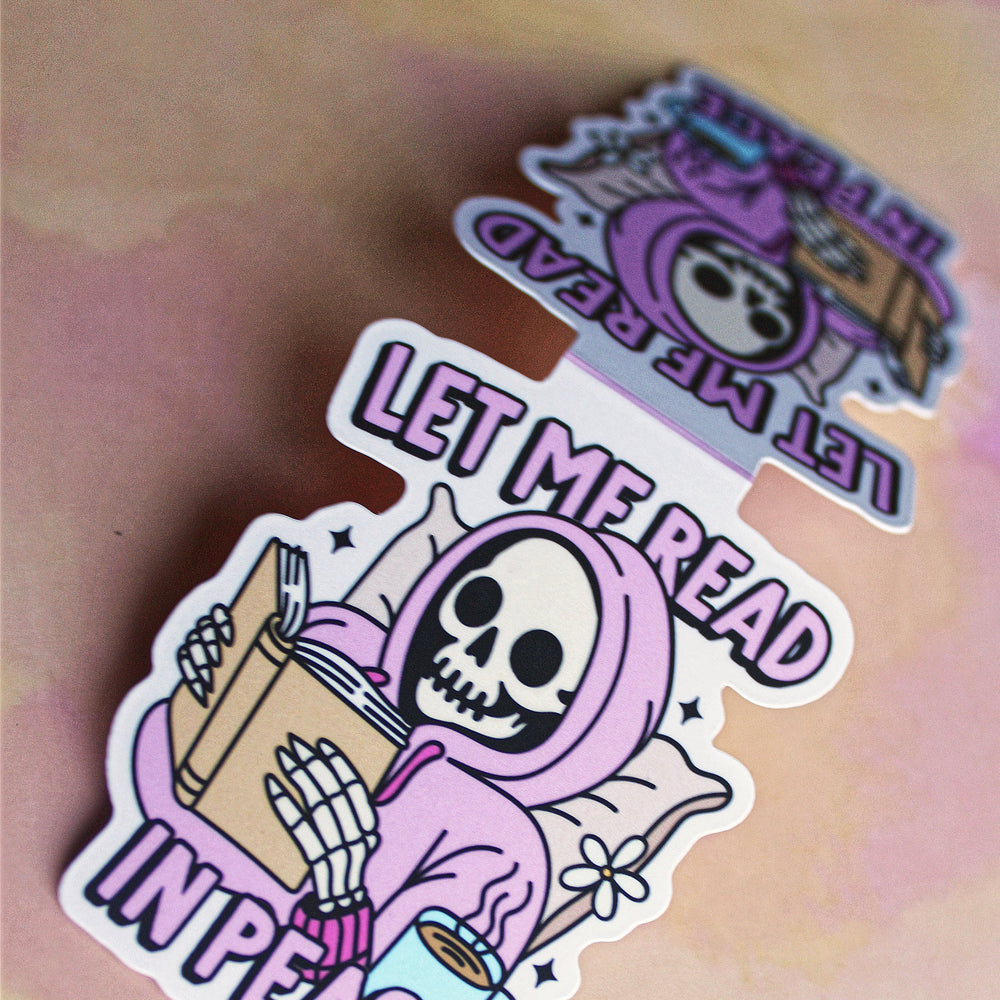 bookmark with a skeleton holding books and text 'Let Me Read In Peace' on a light brown background.