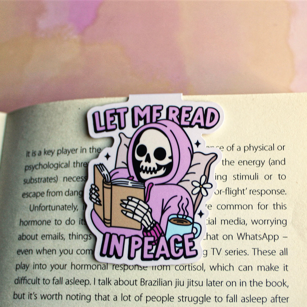 Skull character in a pink hoodie holding a book and a cup of coffee, with 'Let Me Read In Peace' text on a blurred book background.