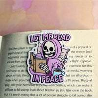 Load image into Gallery viewer, Skull character in a pink hoodie holding a book and a cup of coffee, with 'Let Me Read In Peace' text on a blurred book background.
