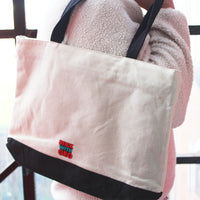 Load image into Gallery viewer, Beige tote bag with black strap held by a person wearing a pink fleece jacket.
