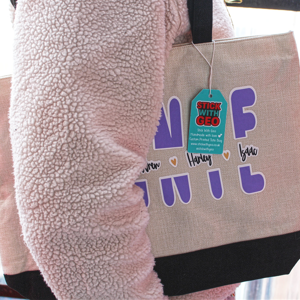 Tote bag with text and a tag, held by a person wearing a pink fleece jacket.