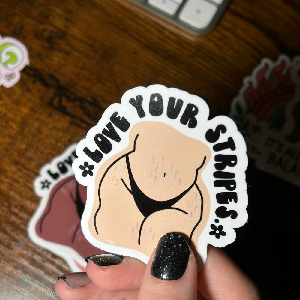 Sticker with 'Love Your Stripes' text held by a hand on a wooden surface