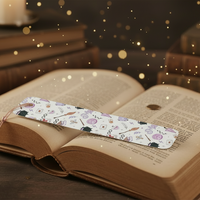 Load image into Gallery viewer, Open book with a decorative bookmark on a dark surface with candles and books in the background
