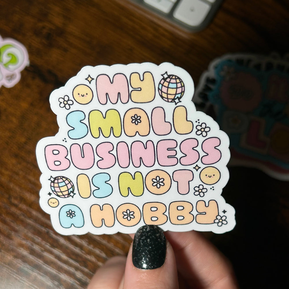 Sticker with 'My small business is not a hobby' text held by a hand on a wooden surface.