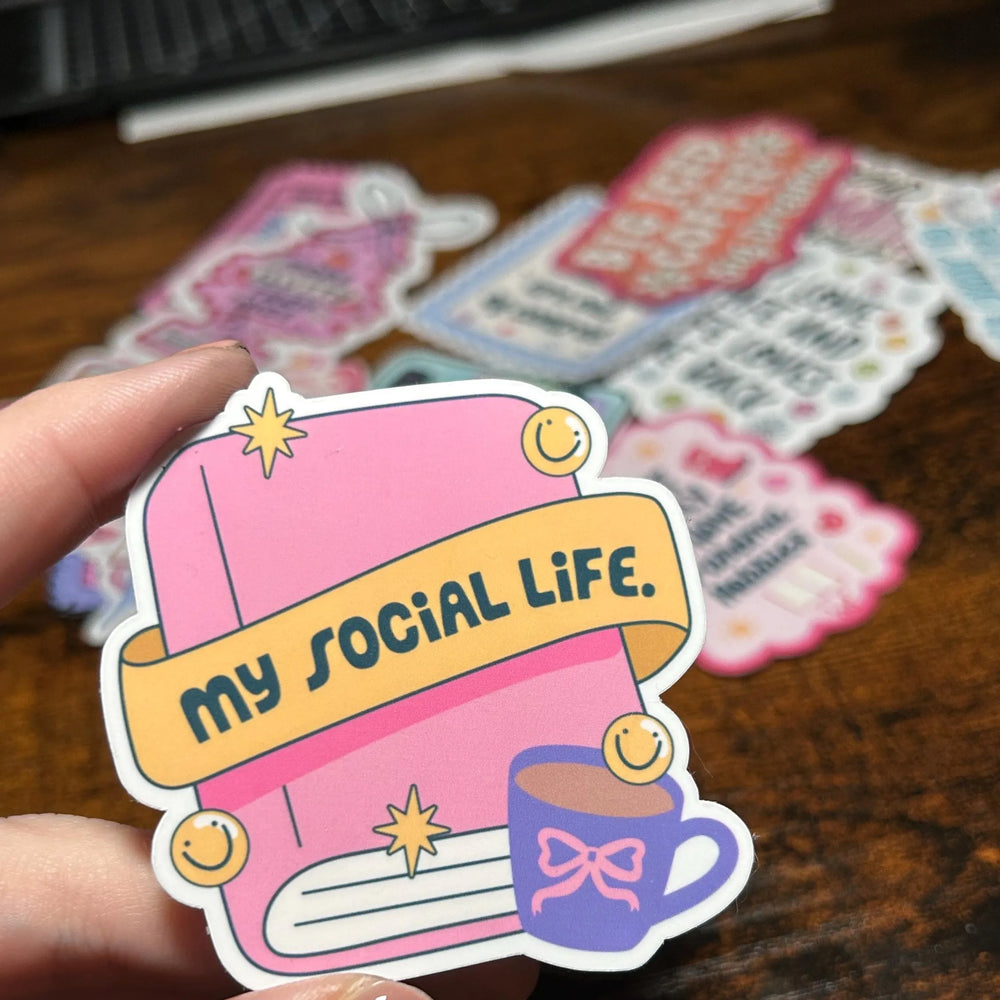 Sticker with 'my social life' text held by a hand on a wooden surface