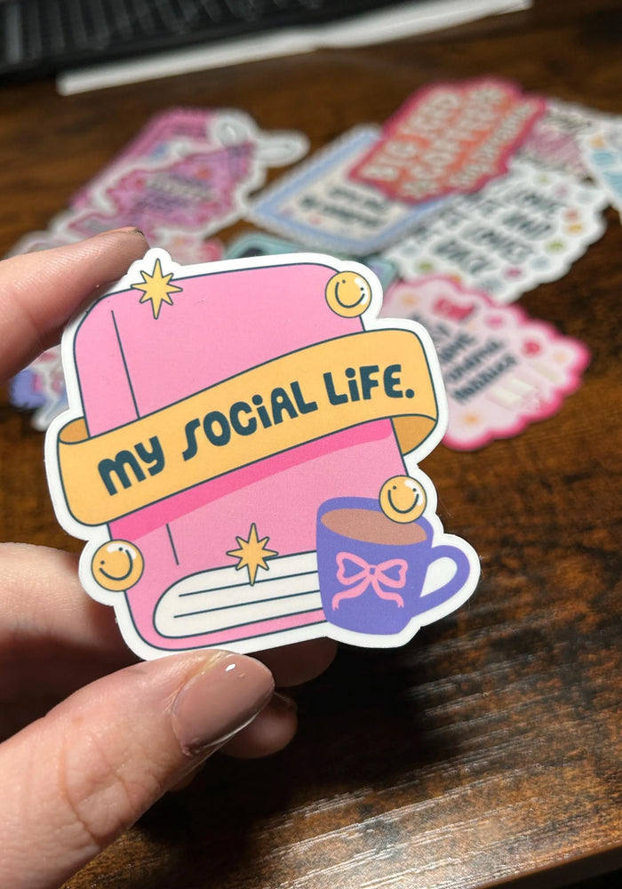 Sticker with 'my social life' text held by a hand on a wooden surface