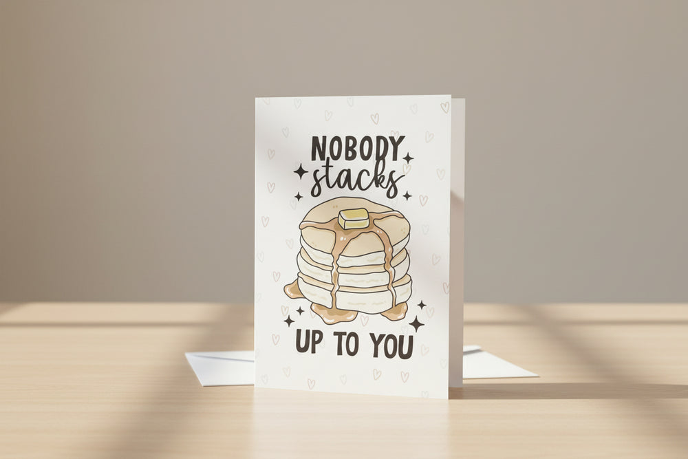 Greeting card with pancakes and text 'Nobody stacks up to you' on a wooden surface.