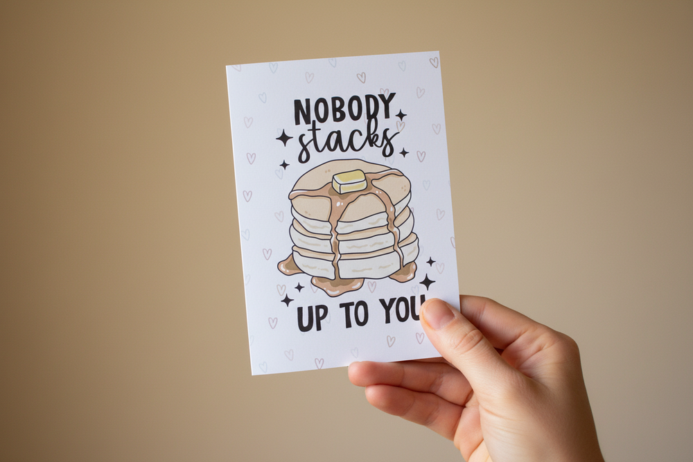 Hand holding a card with a stack of pancakes and text on a beige background