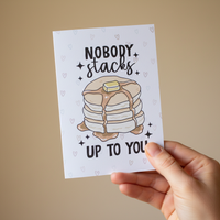 Load image into Gallery viewer, Hand holding a card with a stack of pancakes and text on a beige background
