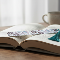 Load image into Gallery viewer, Open book with a bookmark on a wooden table, next to a cup and plant.
