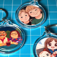 Load image into Gallery viewer, Three keychains with cartoon illustrations of people on a blue grid background
