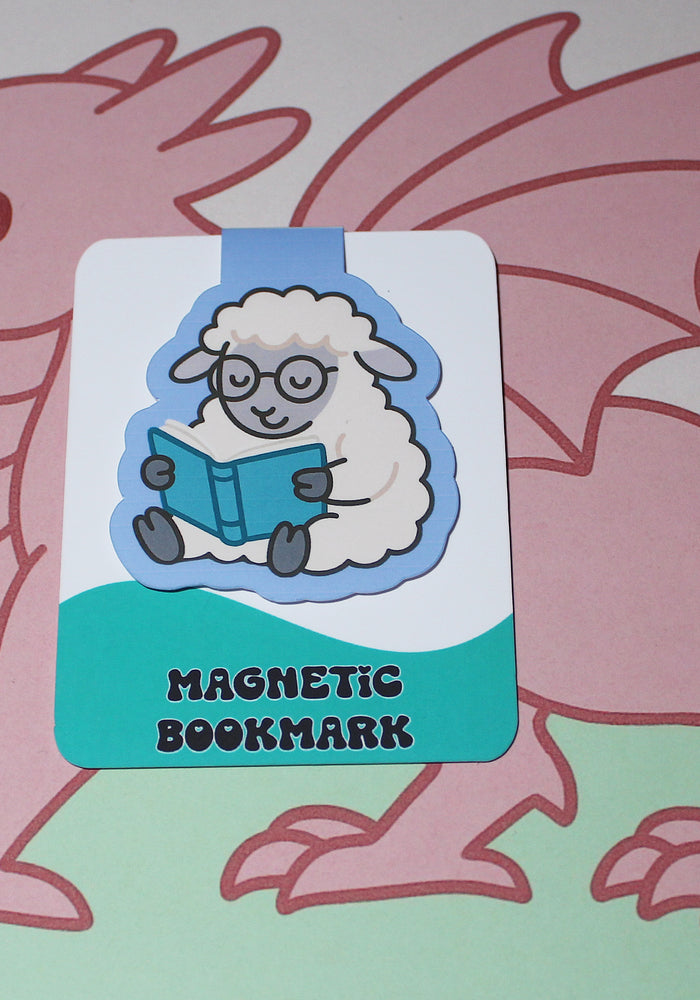 Magnetic bookmark with cartoon sheep reading a book, held by a pink dragon on a light green background