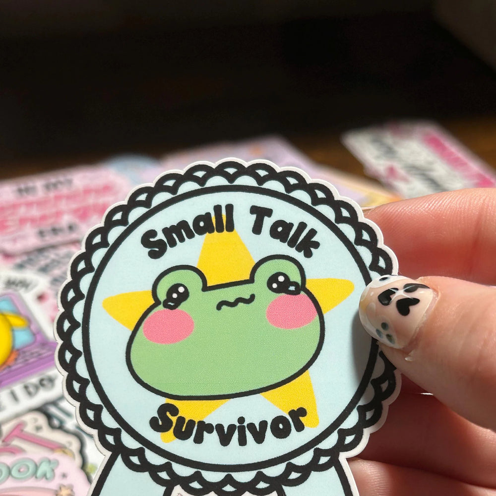 Sticker with a frog design and 'Small Talk Survivor' text held by a hand.