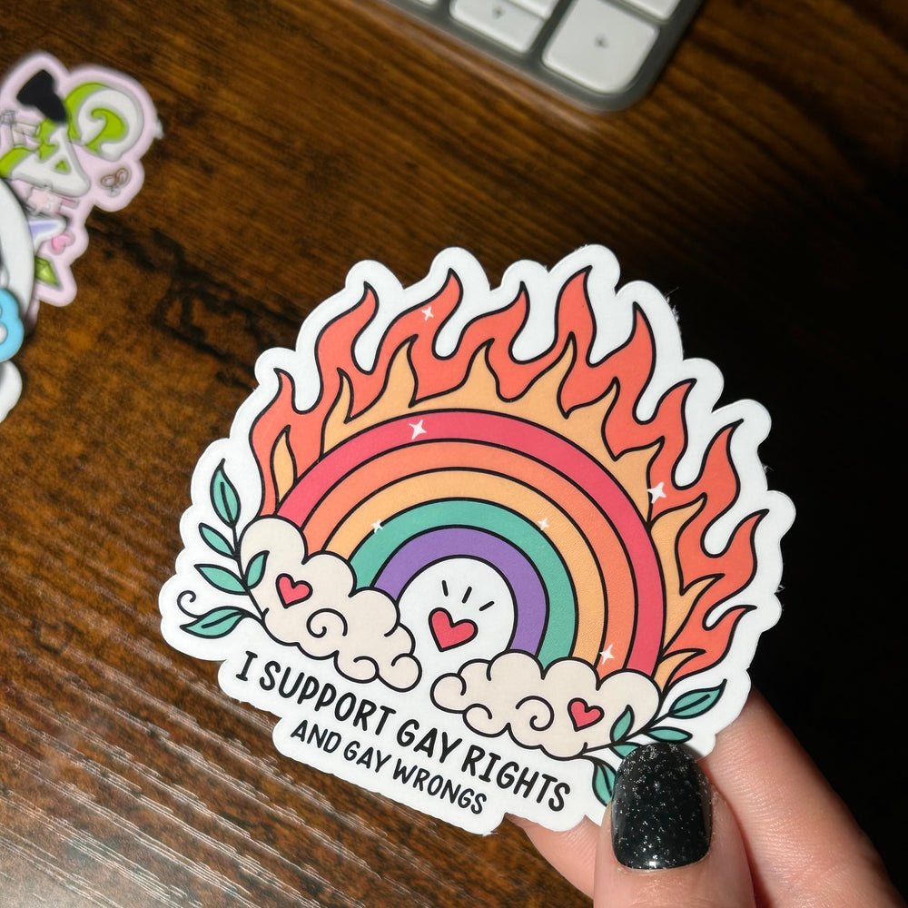 Sticker with rainbow design and text held by a hand on a wooden surface