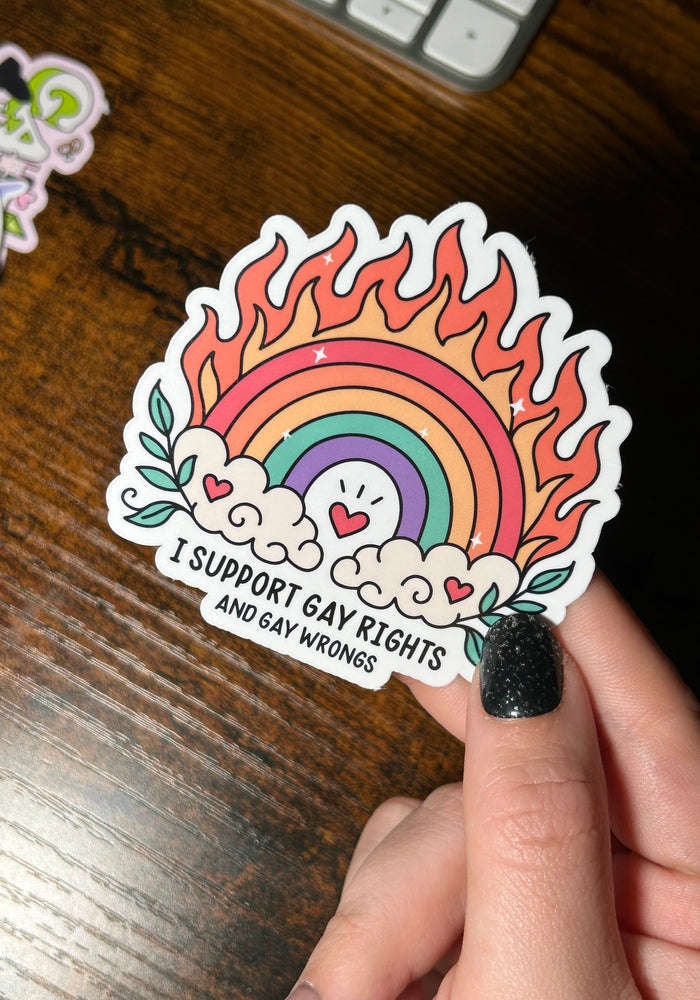 Sticker with rainbow design and text held by a hand on a wooden surface