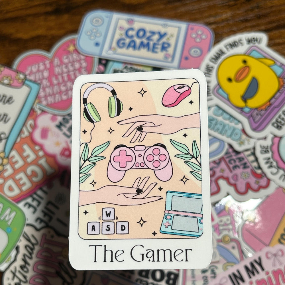 Sticker with 'The Gamer' design surrounded by other colorful stickers on a wooden surface
