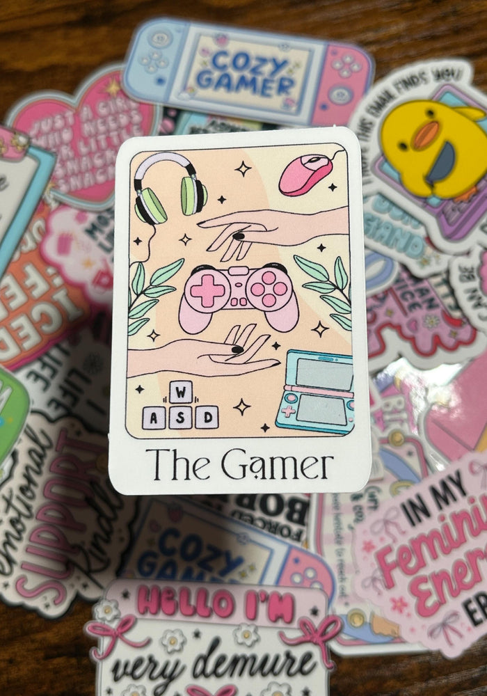 Sticker with 'The Gamer' design surrounded by other colorful stickers on a wooden surface