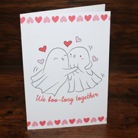 Load image into Gallery viewer, Greeting card with ghost couple illustration and 'We boo-long together' text on a wooden surface
