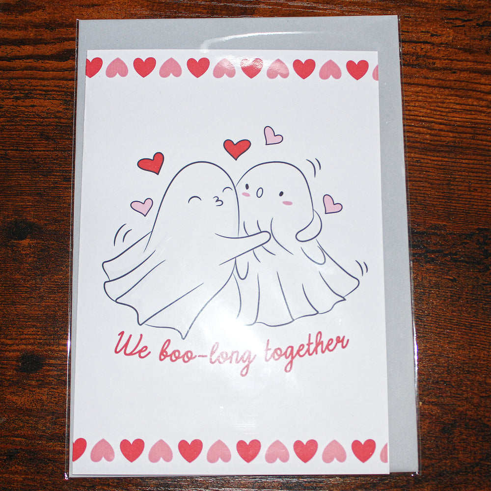 Greeting card with two ghosts hugging and hearts on a wooden surface