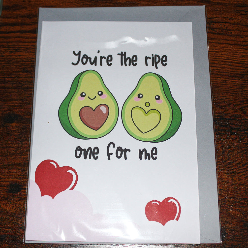 Card with cartoon avocados and text 'You're the ripe one for me' on a wooden surface