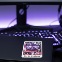 Load image into Gallery viewer, A square sticker with a colorful cartoon illustration and the text 'The Co-Op Gamer' is shown on the lid of a black laptop. The laptop sits on a desk in front of a blurred computer keyboard and monitor with purple backlighting.
