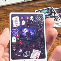Load image into Gallery viewer, A hand holding a rectangular Sticker titled "The Horror Gamer" with a dark purple illustrated scene featuring a computer setup, ghosts, a mask, and gaming-themed graphics. Other Stickers are partially visible on a wooden tabletop.
