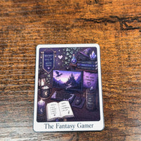 Load image into Gallery viewer, A tarot sticker titled 'The Fantasy Gamer' featuring a whimsical illustration of a cozy gaming setup with a fantasy theme, placed on a rustic wooden surface.
