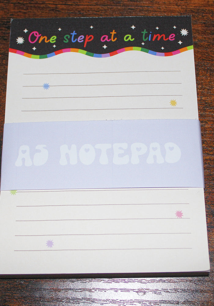Notepad with 'One step at a time' text on a wooden surface