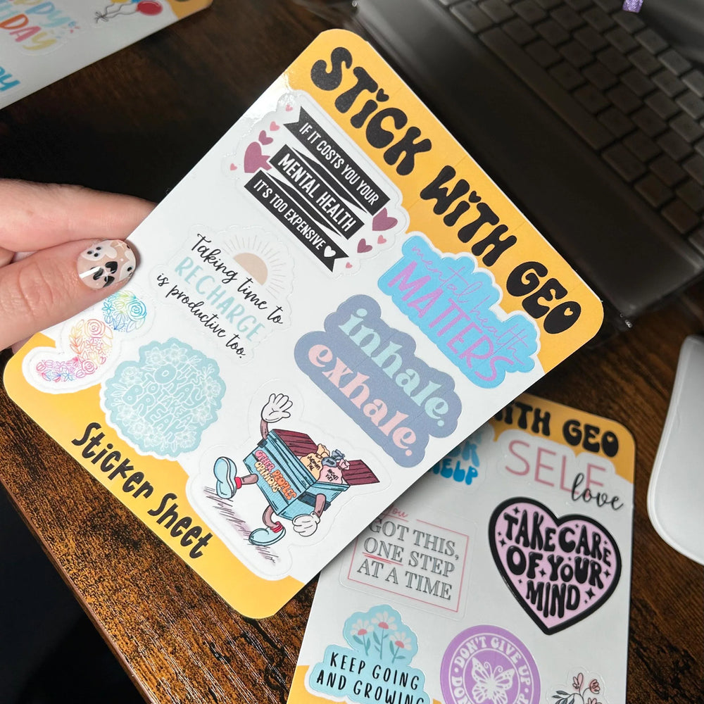 Sticker sheets with motivational phrases held by a hand on a wooden surface