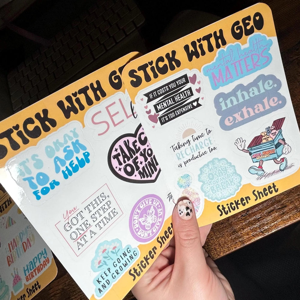 Sticker sheet with various designs and text held by a hand on a wooden surface.